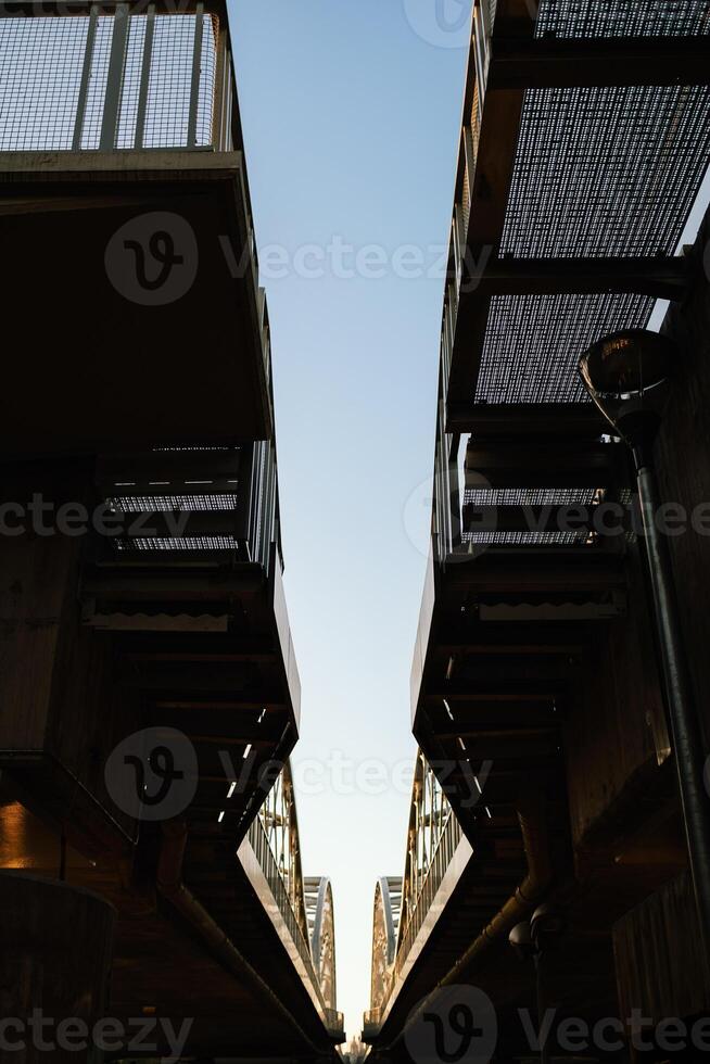 Converging lines of pedestrian bridge creating symmetrical composition against clear sky during sunset, with metal grid flooring and railings, offering unique perspective on urban infrastructure photo