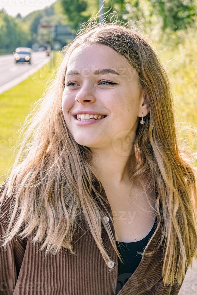 A young woman with long blonde hair smiles in front of a highway photo