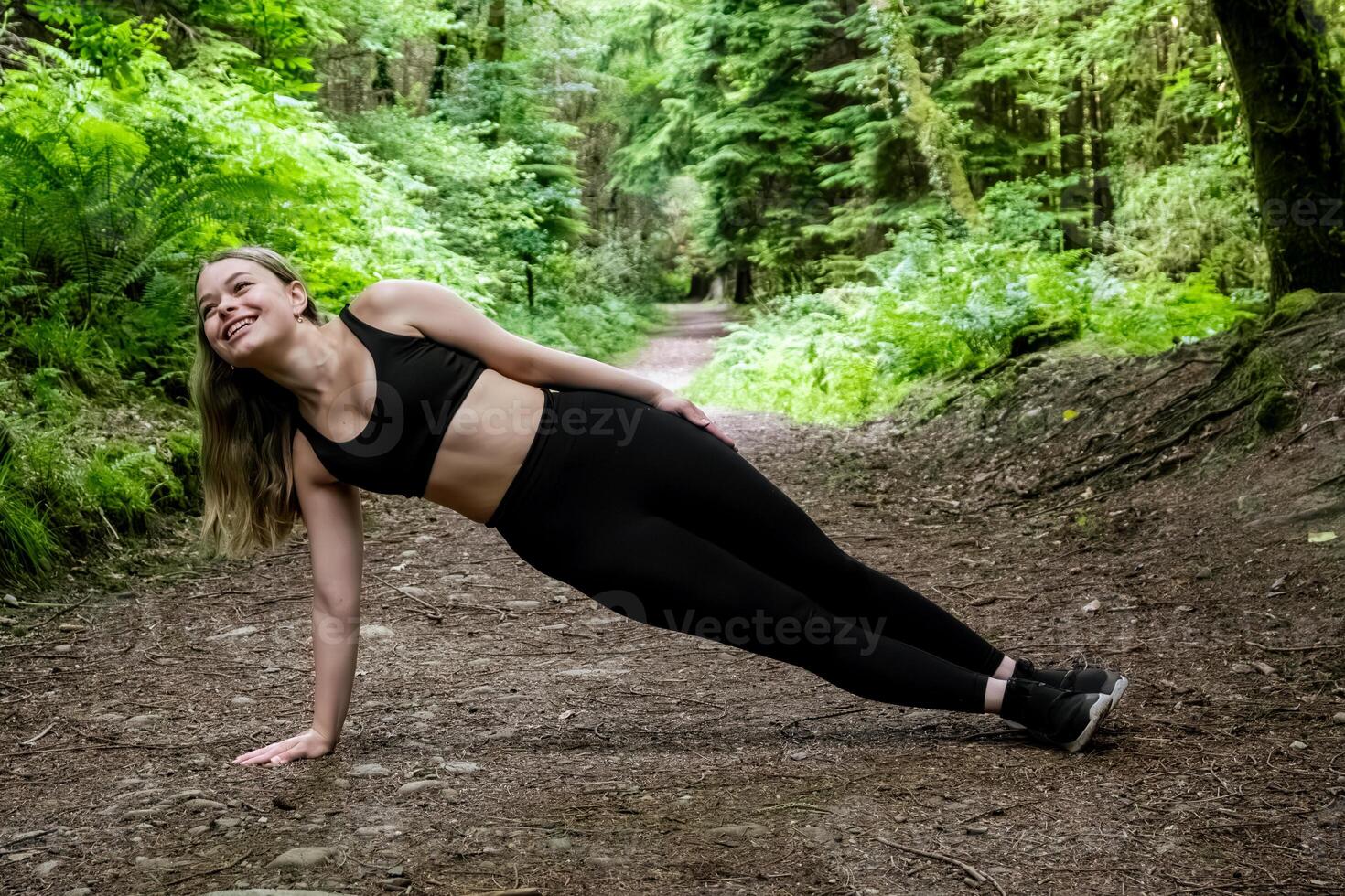 A woman is performing a challenging side plank on a dirt path in the woods photo