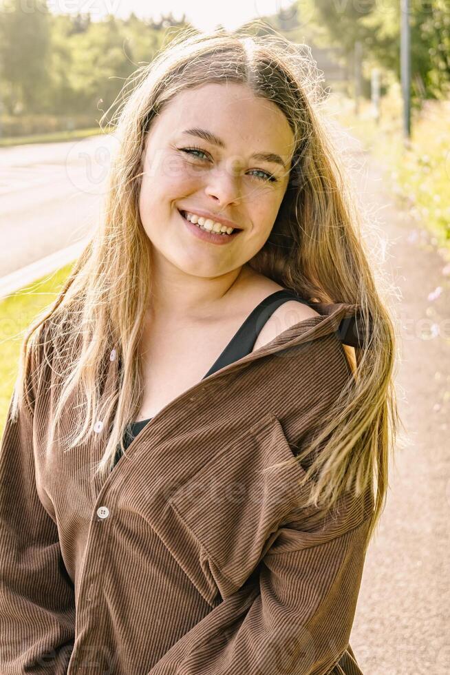 A Smiling Young Woman in Nature Wearing a Brown Jacket amidst a Beautiful Setting photo