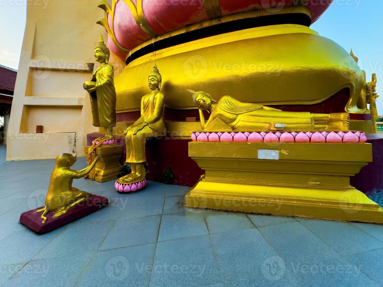 This low-angle, wide-shot captures a collection of resplendent golden Buddha statues, depicting various poses including standing, sitting, and reclining, arranged at the base of a large, golden temple photo