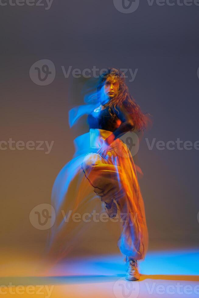 Stylized jazz-funk dancer captured mid-motion with vivid neon lighting, dynamic movement trails, and expressive pose in urban studio setting, showcasing rhythm and energy. photo