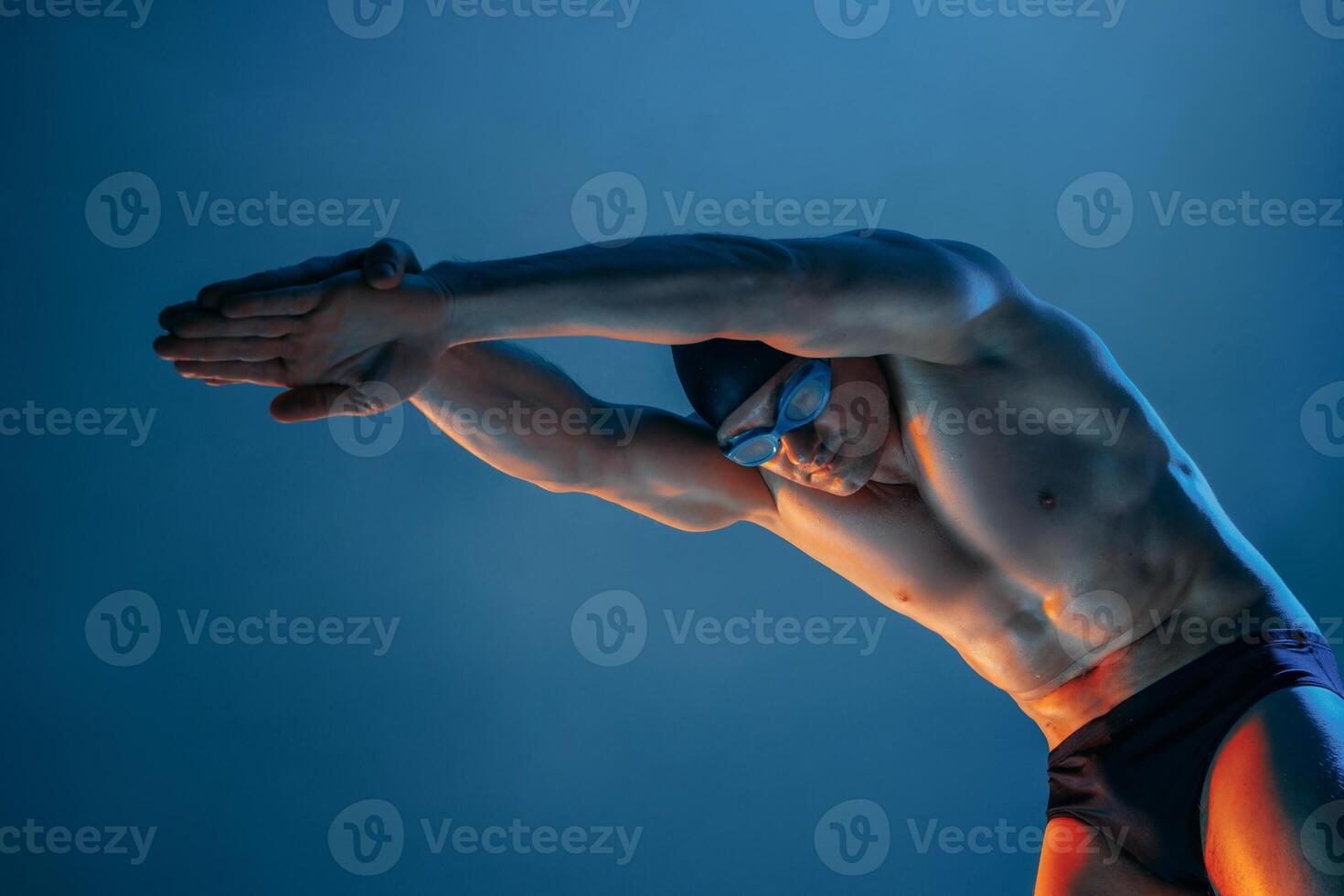 Muscular swimmer in diving stance, arms forward, under dramatic lighting in studio setup. photo