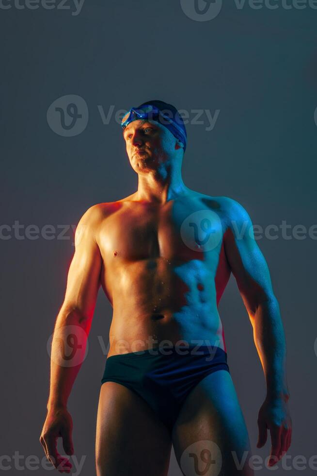 Confident male swimmer poses under blue and orange lights, ready for competitive action. photo