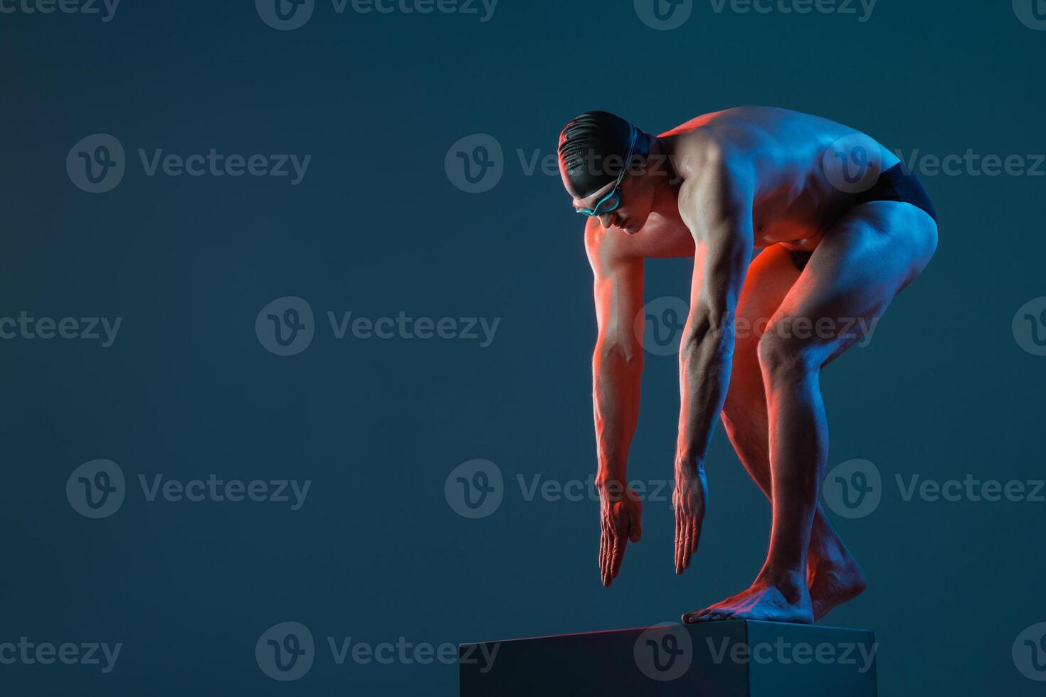 Swimmer ready to dive from block, intense side lighting, athletic pose in studio setting. photo