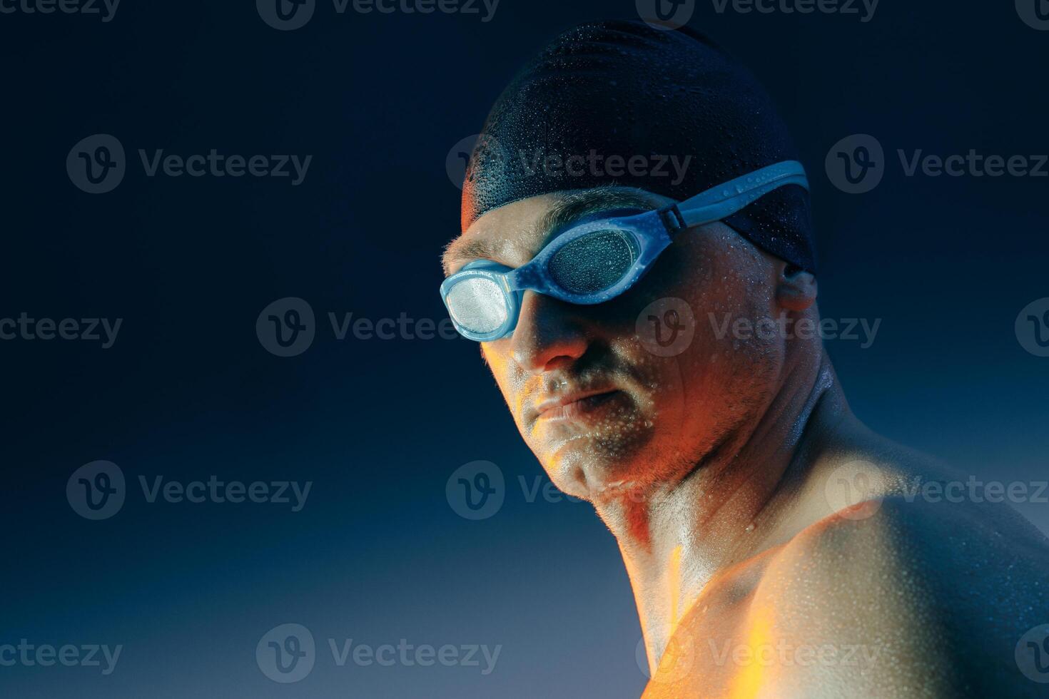 Determined swimmer wearing goggles and cap, highlighted by blue and orange studio lighting. photo