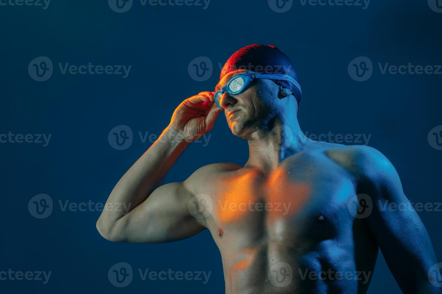 Focused swimmer in goggles and cap, lit by contrasting lights, ready to dive into action. photo