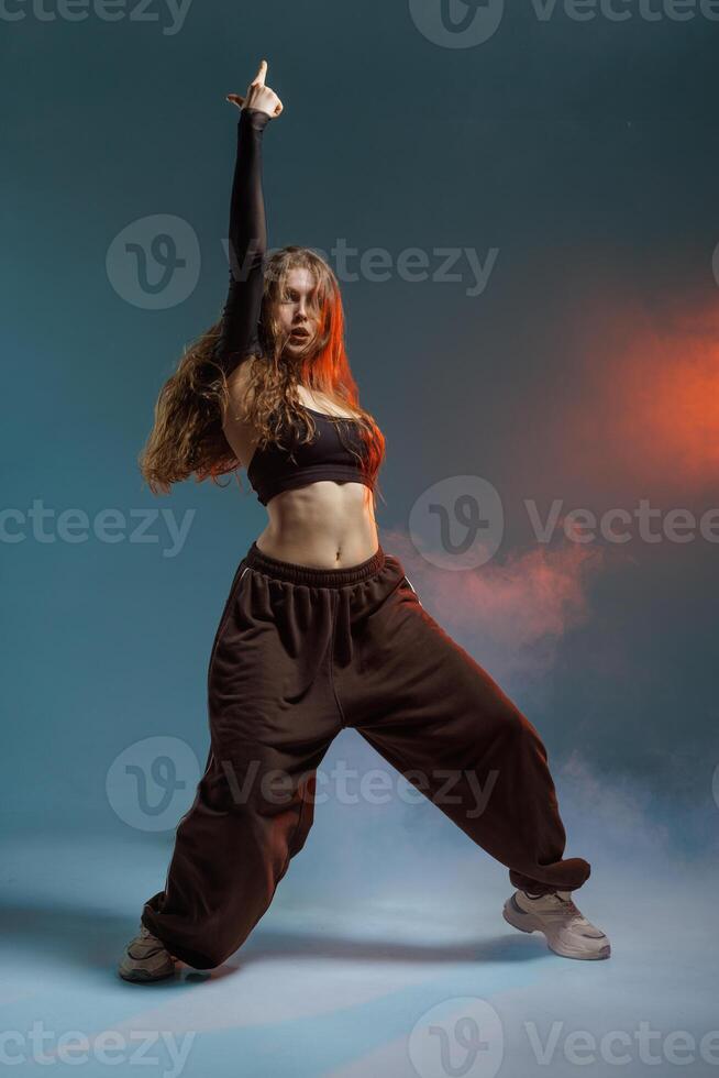 Confident jazz-funk dancer strikes a powerful pose in dramatic studio lighting with smoke effects, showcasing strength, rhythm, and bold street dance attitude. photo