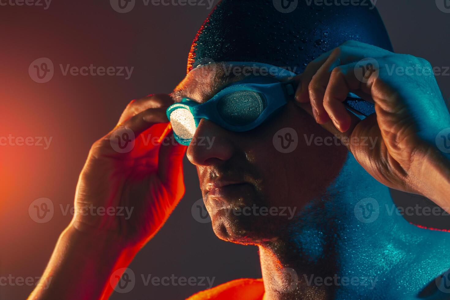 Swimmer adjusts goggles, water droplets and dramatic lighting show focus before race. photo
