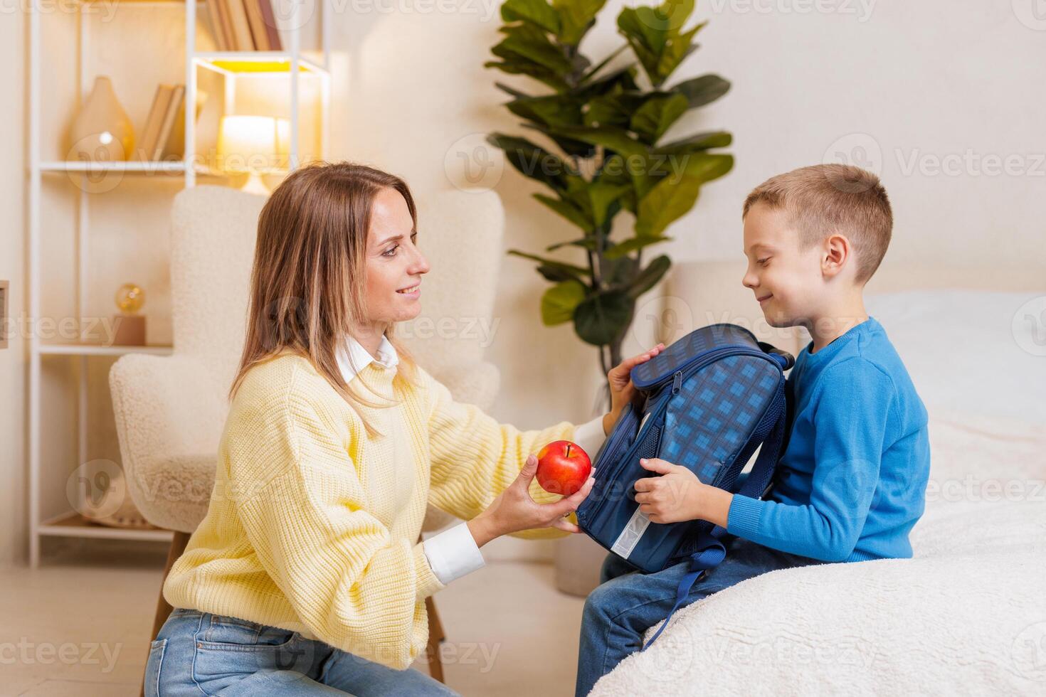 Mother Gives Son an Apple While Packing School Backpack Back to School Morning Preparation at Home photo