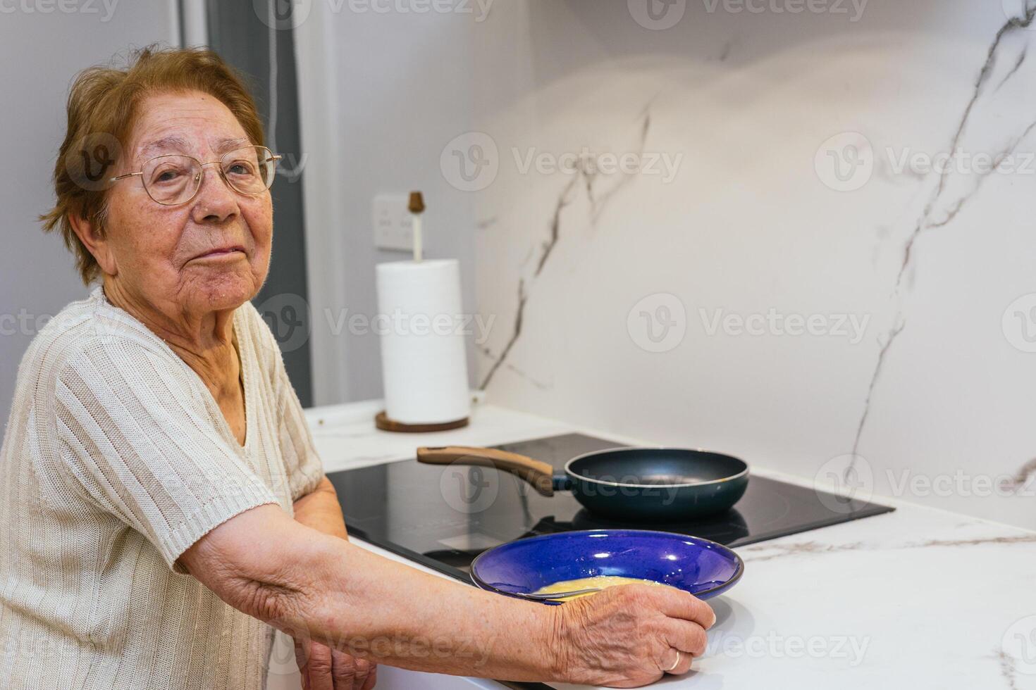 Elderly woman preparing scrambled eggs in modern kitchen photo