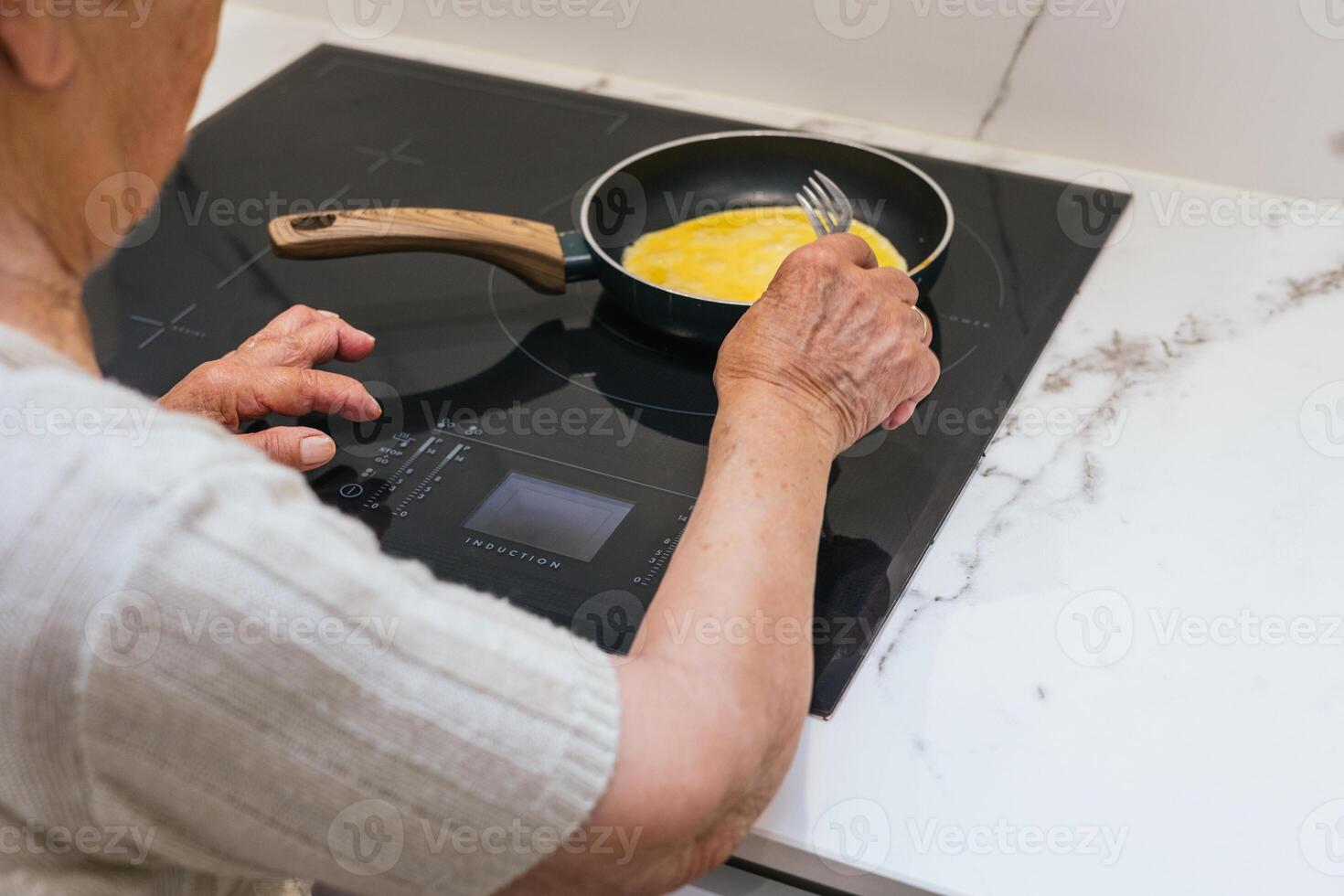 Elderly woman cooking scrambled eggs on induction hob photo