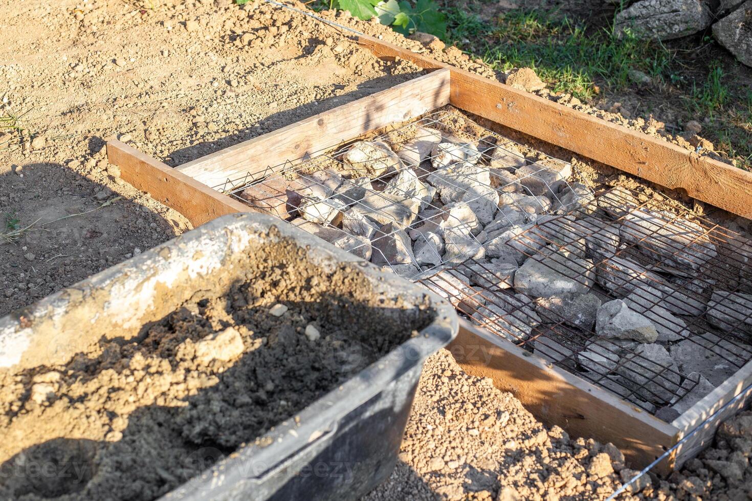 black tub filled with a mixture of sand and water sits next to a construction site prepared with rocks and wire mesh for pouring concrete photo