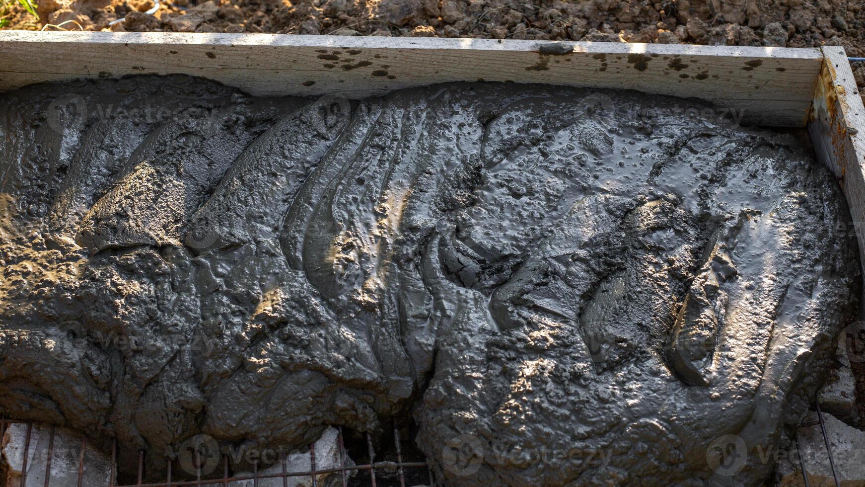 Wet concrete poured on a foundation of stones reinforced with wire mesh in a timber frame. Construction of a foundation photo