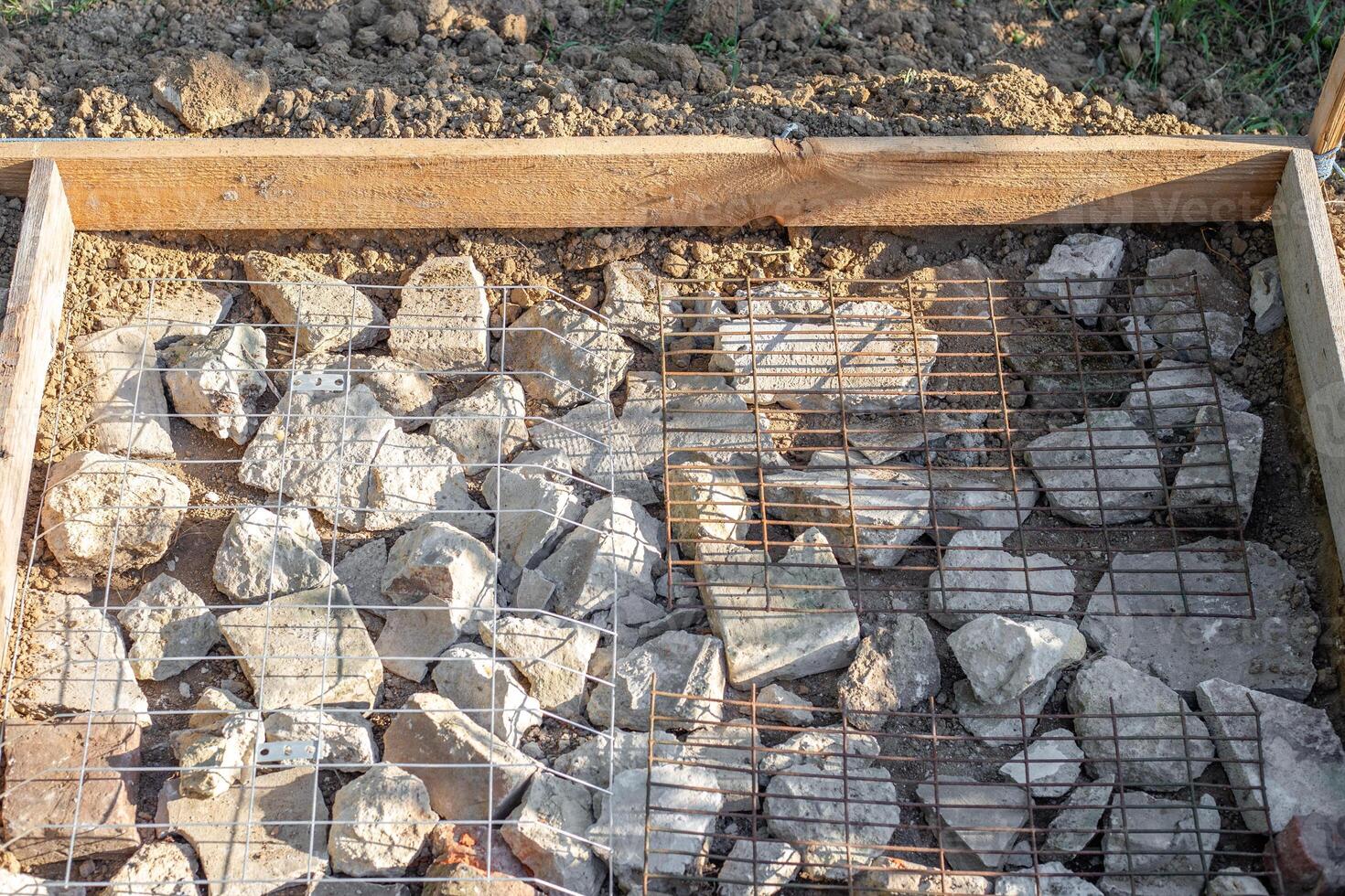 A construction site is prepared with rocks and wire mesh in a timber frame for pouring a concrete slab photo