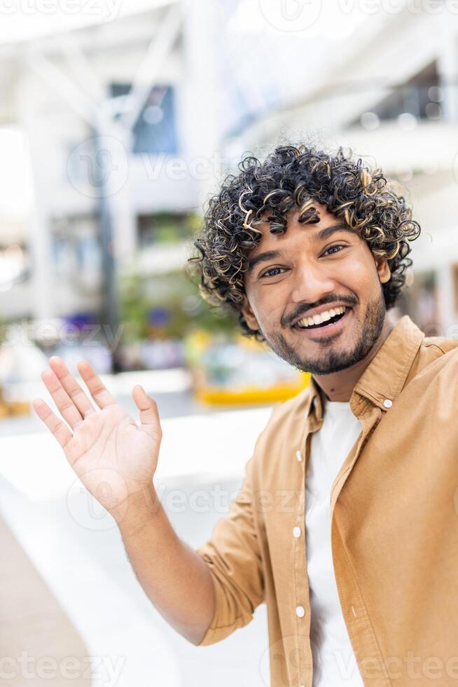 An attractive man waves hello in a call using his phone, smiling brightly photo