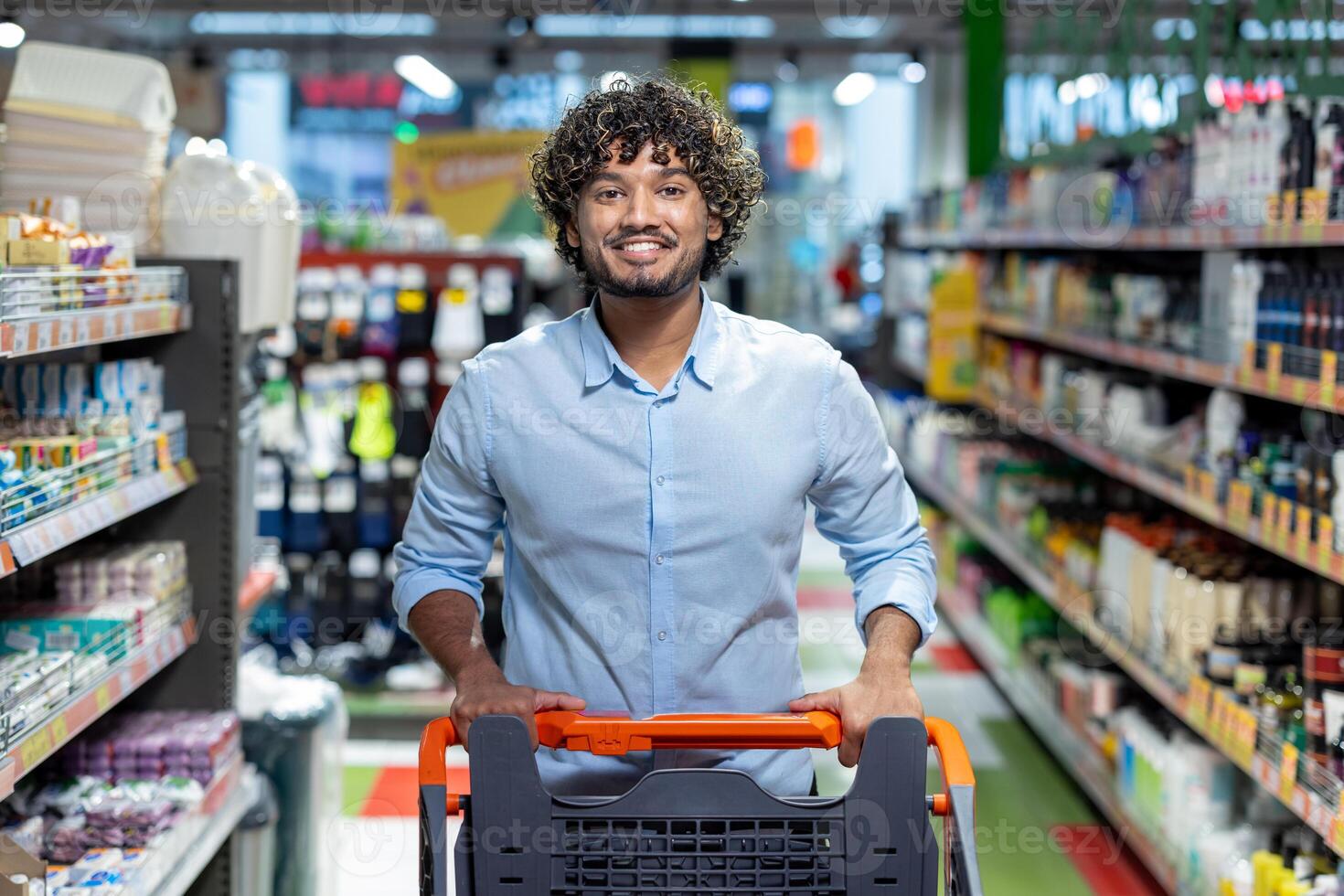 A smiling man pushes a shopping cart down an aisle in a brightly lit grocery store, focused on purchasing. photo