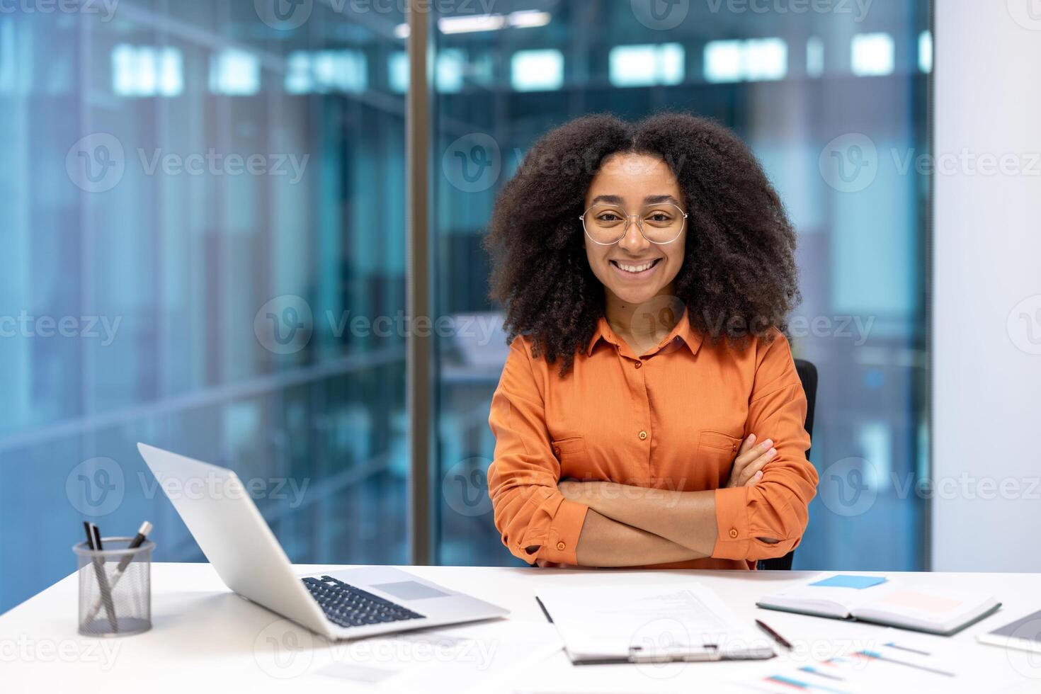 A smiling businesswoman with crossed arms sits in a modern office, radiating confidence and approachability. photo
