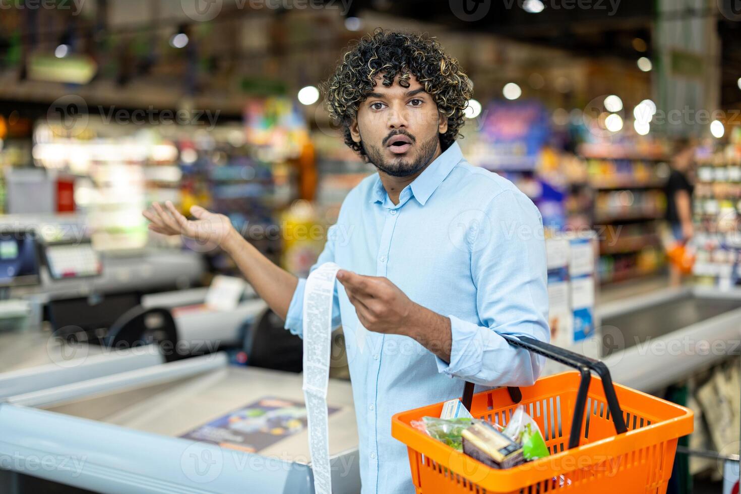 A shocked man looks at his grocery bill, holding a shopping basket in a supermarket. He is surprised by the total. photo