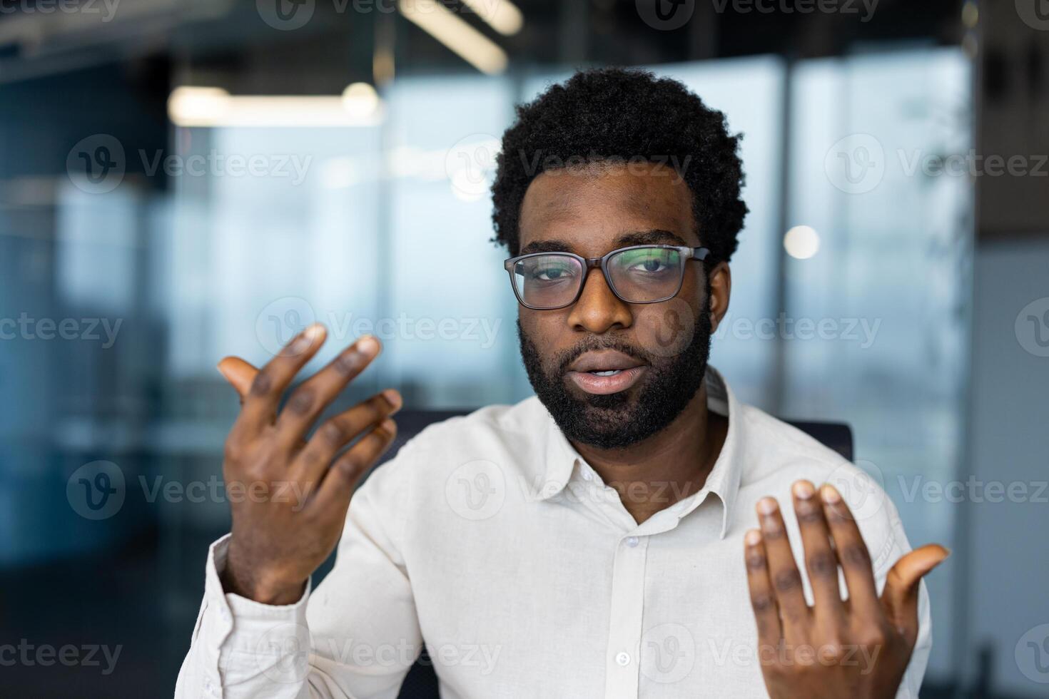 A man with glasses gestures during a conference. He appears to be discussing something, hands moving. photo