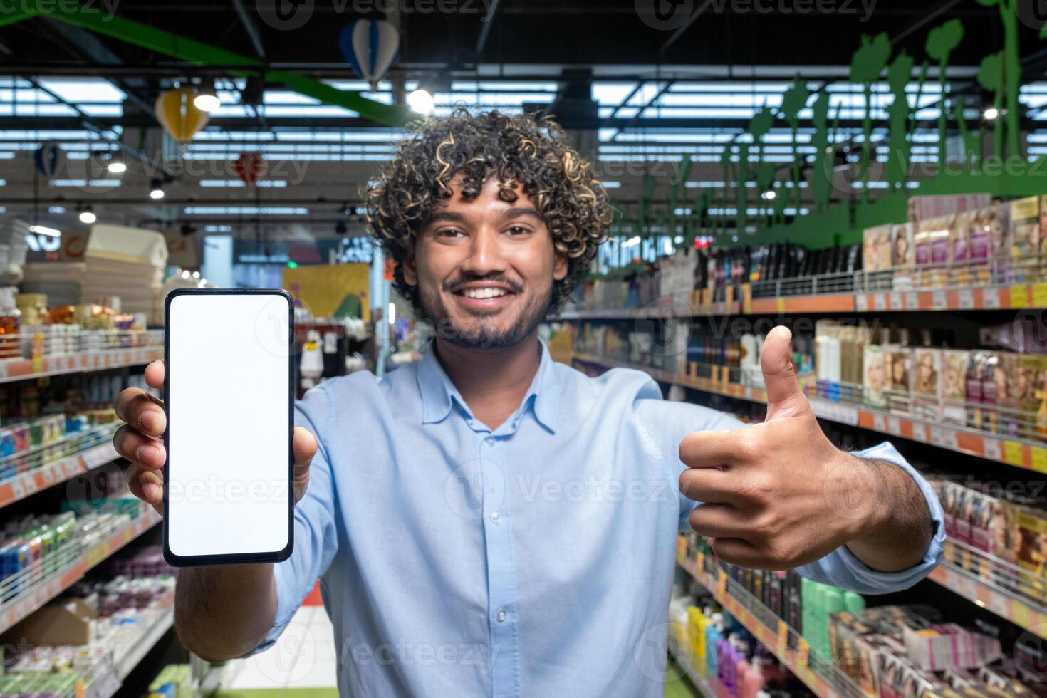 A man holding a phone with a blank screen in a supermarket, giving a thumbs-up, promoting online shopping. photo
