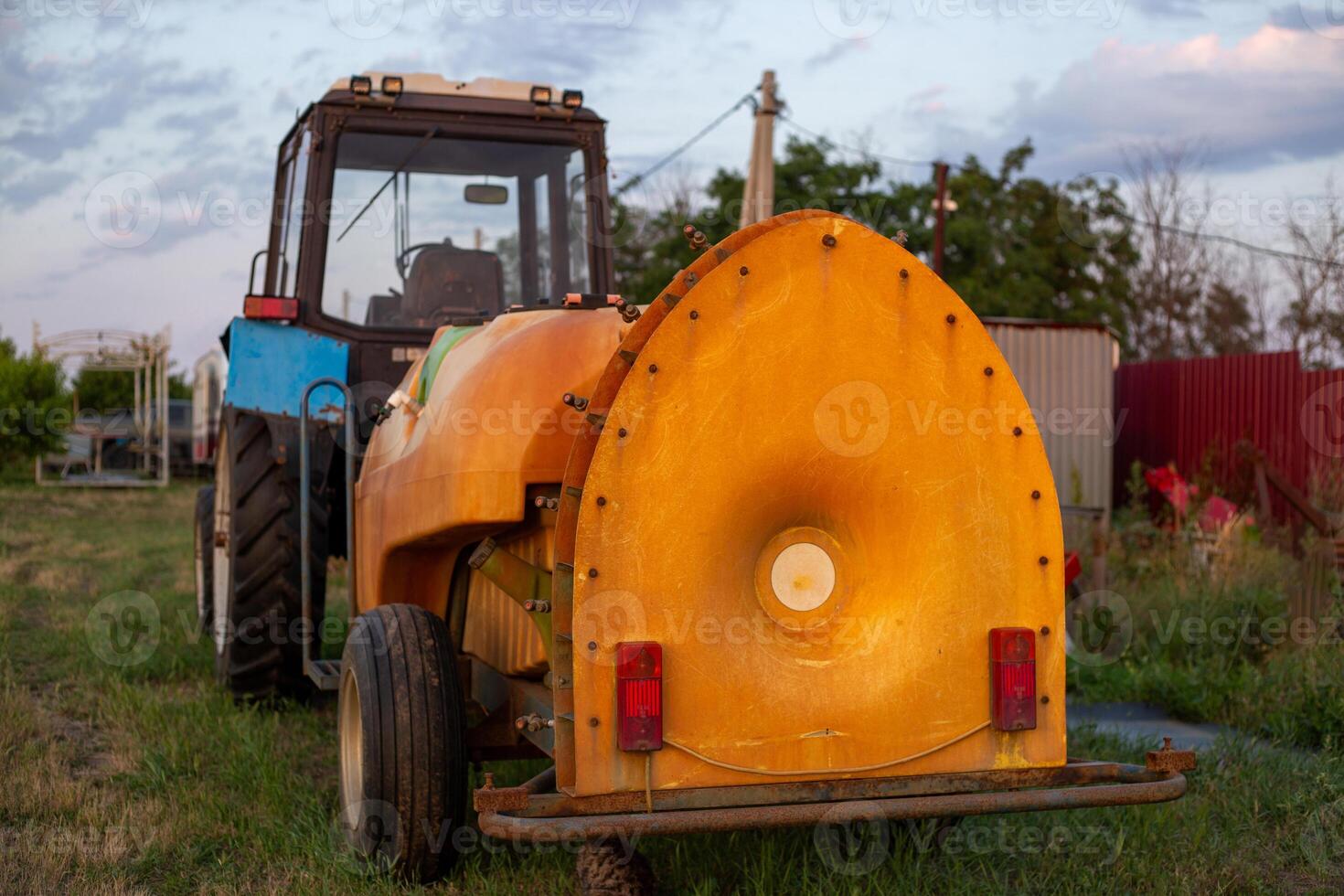 Blue tractor and orange agricultural sprayer on grassy field. Farm machinery for agricultural work photo