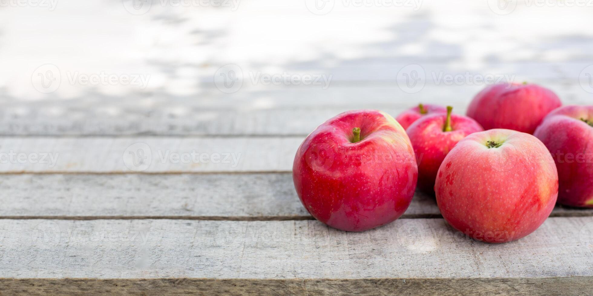 A bunch of bright red apples on a weathered wooden surface with soft lighting and enough space for text photo