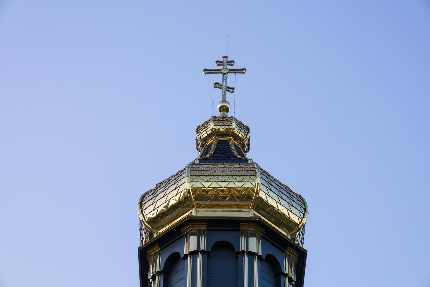 A stunning golden dome adorned with a cross rises above an old church, framed by a bright blue sky during a sunny day photo