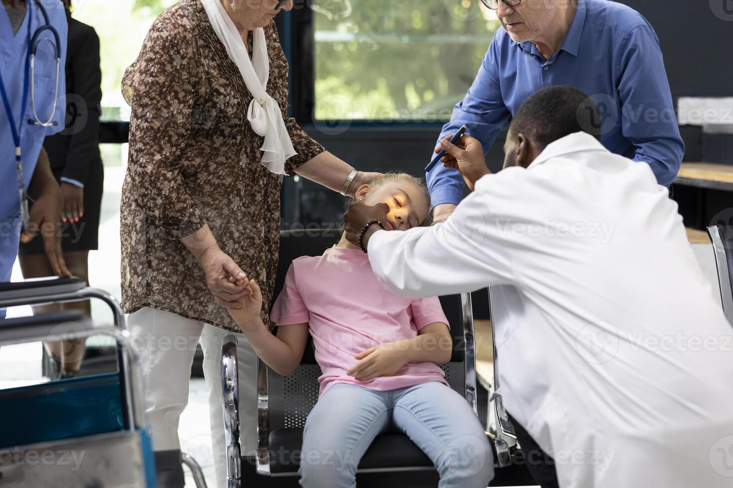 Unconscious child causes alarm for senior grandparents at clinic, black doctor consulting and offering support to young kid during urgent pediatric health scare. Helps with first aid. photo