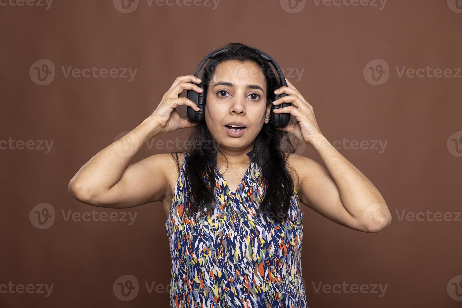 Portrait of female model wearing headphones, reacting to surprising audio content with an expressive face. Astonished woman with wide eyes and open mouth stares at camera, stunned by what she hears. photo
