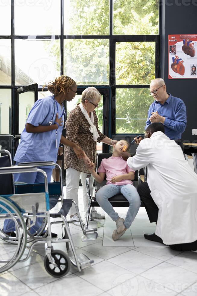 Family emergency unfolds as small girl collapses in hospital lobby with senior grandparents seeking diagnosis and assistance from healthcare professionals during critical pediatric situation. photo