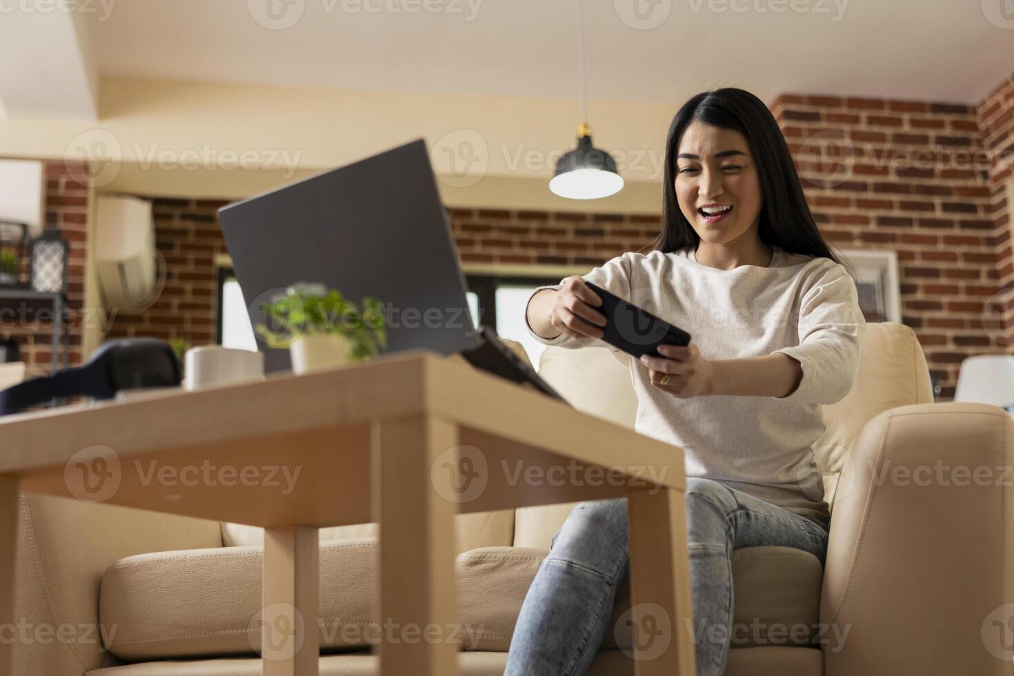 Excited remote female manager taking pause on work, playing games on cellphone. Cheerful businesswoman resting and enjoying mobile gaming entertainment in brick wall apartment. photo