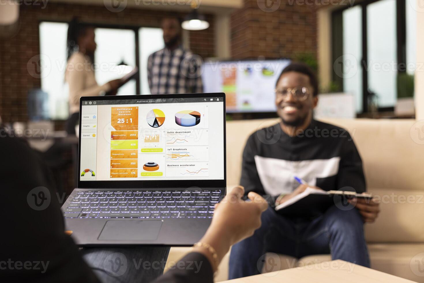 African american entrepreneur holding laptop showing company analytics, reviewing marketing strategy with male coworker. Selective focus on device held by businessperson, showing performance graphs. photo