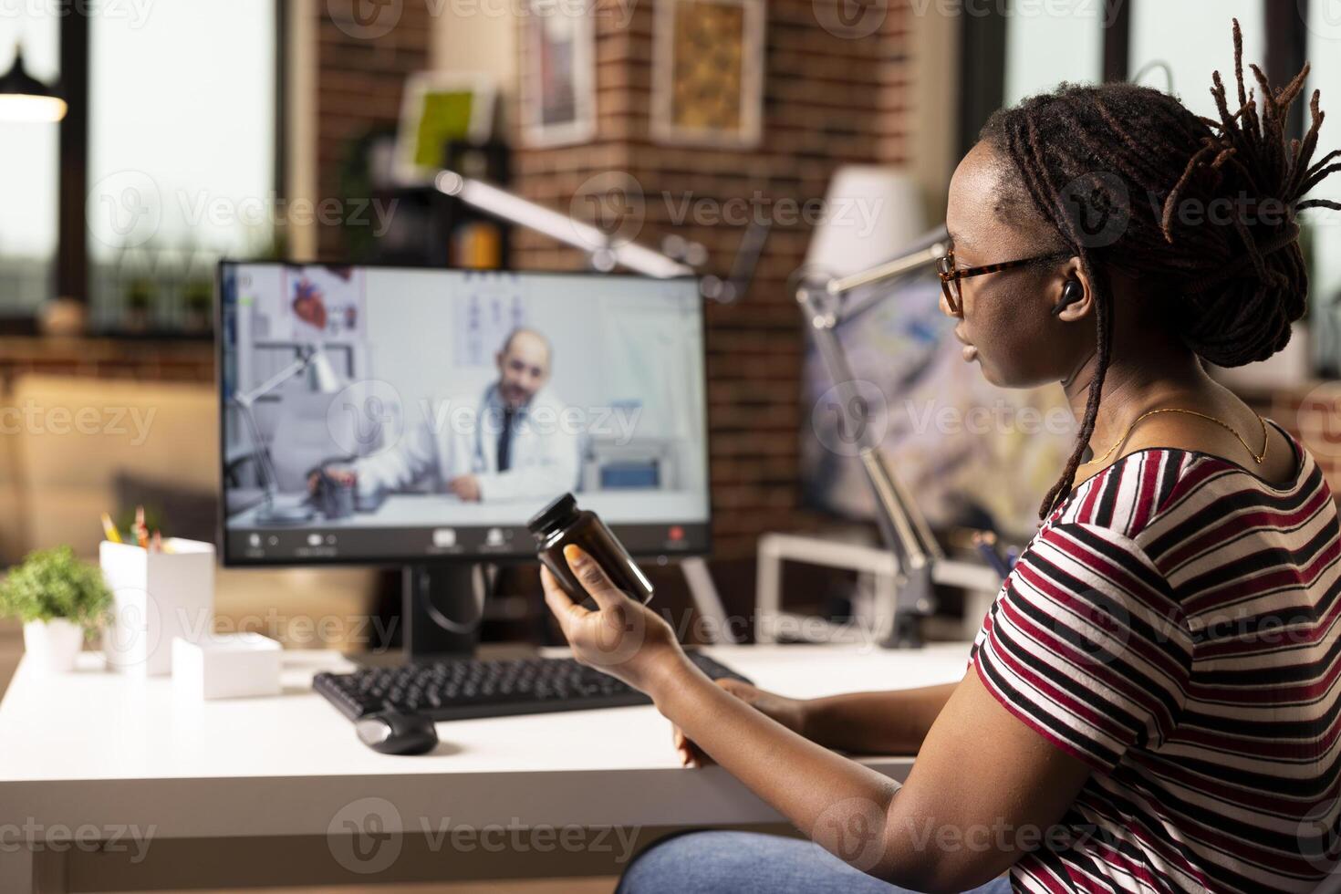 African american woman seated at desk talking to caucasian doctor on call. Black female entrepreneur holds pill bottle, discussing prescription and treatment during online medical consultation. photo