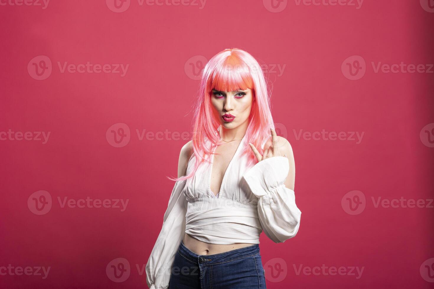 Beautiful caucasian woman with pink hair and pursed lips, flashing playful rock hand gesture. Fashionable young lady expresses bold personality against pink background in energetic studio portrait. photo