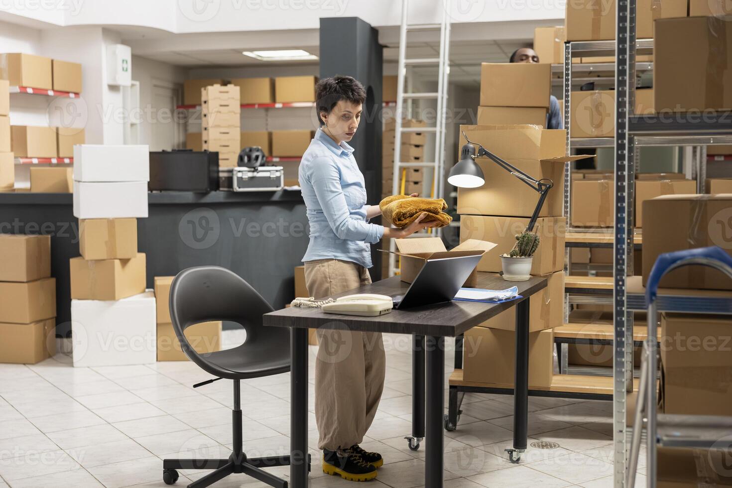Woman depot worker preparing boxes for shipment in local brand supply room, managing the orders on a laptop. Fulfillment center focused on retail operations and e commerce distribution. photo