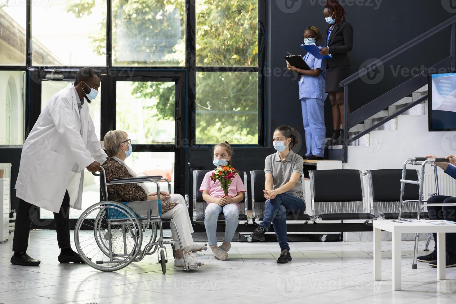 Little girl offering flowers during visiting hours with grandma in wheelchair, offer bouquet and respecting hospital safety or hygiene standards. Medical regulations to visit patients at hospital. photo