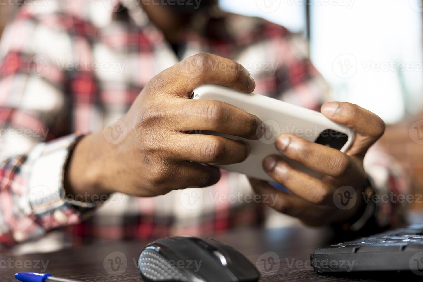 Closeup on hands of black man using mobile device for online gaming entertainment. African american male individual seated at home office desk, playing games on smartphone. photo