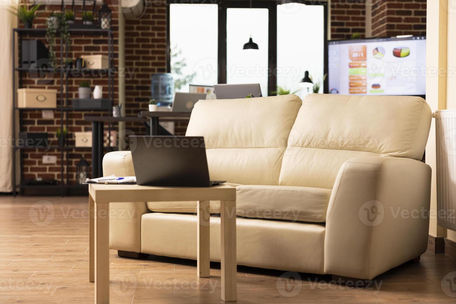 Vacant brick wall workspace neatly organized for employees at startup company. Empty cozy sofa with laptop nearby on table, highlighting comfort and productivity in modern office. photo