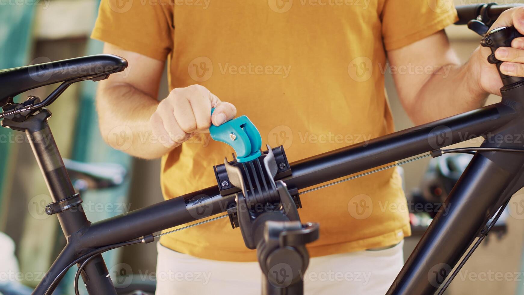 Active caucasian man placing and clamping bicycle body to repair-stand for safe outdoor maintenance. Young person securing and adjusting bike in preparation for servicing in yard. photo