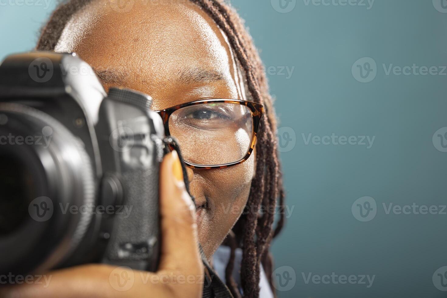 Closeup of black female individual holding DSLR against blue background, showing camera handling techniques. African american professional photographer working in modern studio. photo