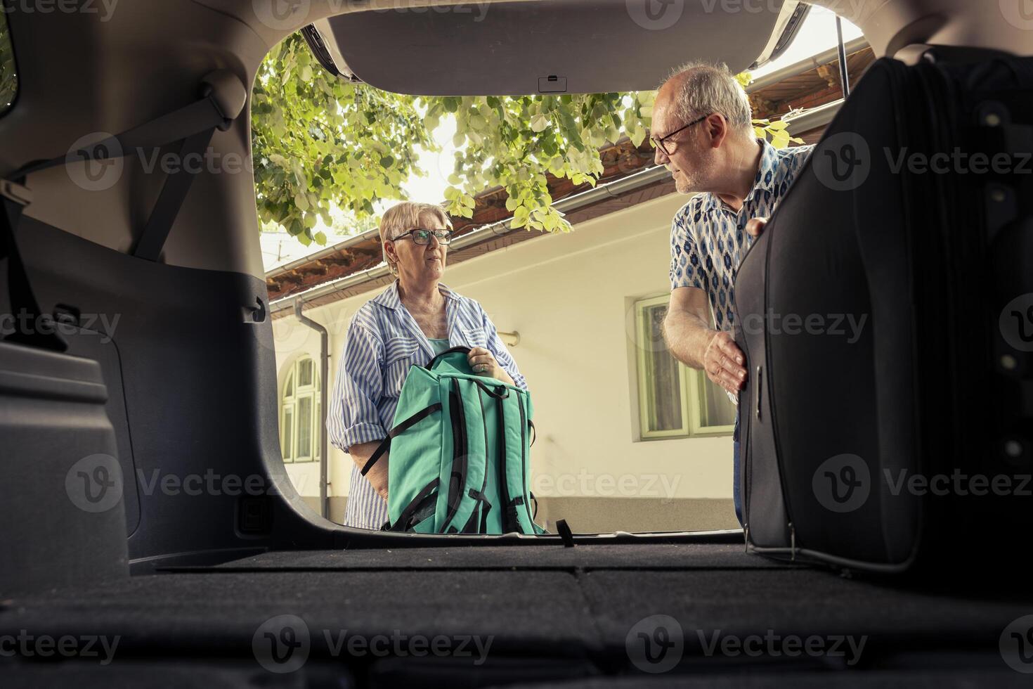 Senior couple loading their luggage in the car trunk for a vacation drive and preparing with road essentials. Retired excited people embrace the free time and comfort of travelling together. photo