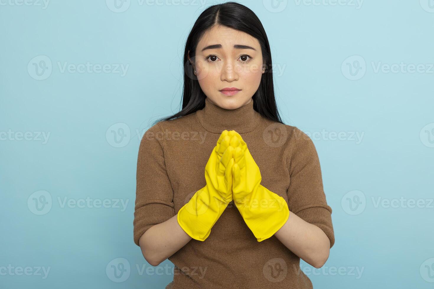 Worried female janitor stands with palms together, apologizing after making cleaning mistake. Asian housekeeper looking at camera with nervous, regretful expression, seeking forgiveness at work. photo