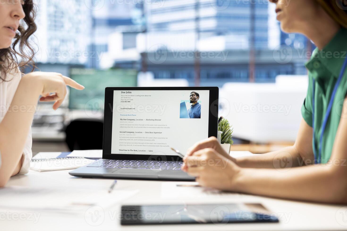 HR manager looking at CVs on tablet to vet selected applicants and ensure their skills match role needs. Headhunters in startup workspace reading resumes on device, assessing candidate work experience photo