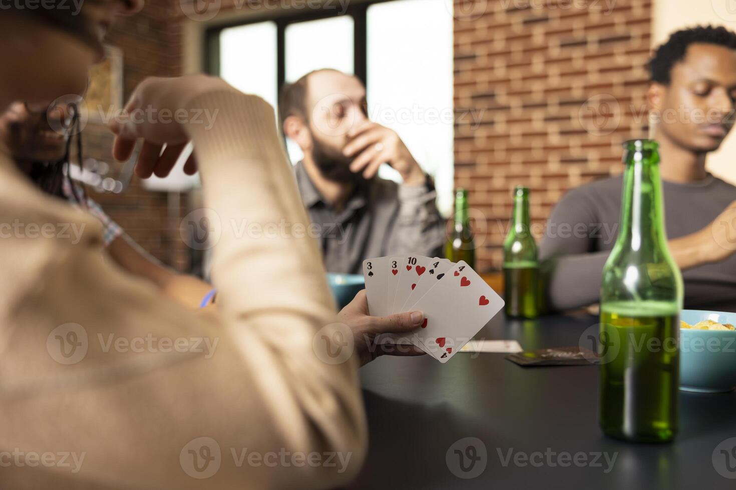 Closeup of woman playing cards with diverse friends, sharing beverages and snacks at home. Happy group playing poker at table with selective focus on deck of cards held by caucasian female individual. photo