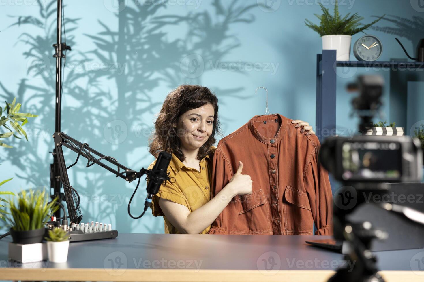 Media star satisfied with orange jacket recently purchased, showing fans, doing thumbs up, filming herself in studio. Content creator in studio presenting new acquisition, doing agreeing hand gesture photo