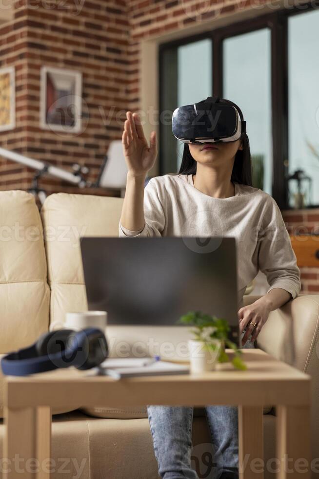 Remote female manager sitting in living room, using vr headset for immersive business planning. Young woman entrepreneur using futuristic tech, checking financial information and online presentations. photo