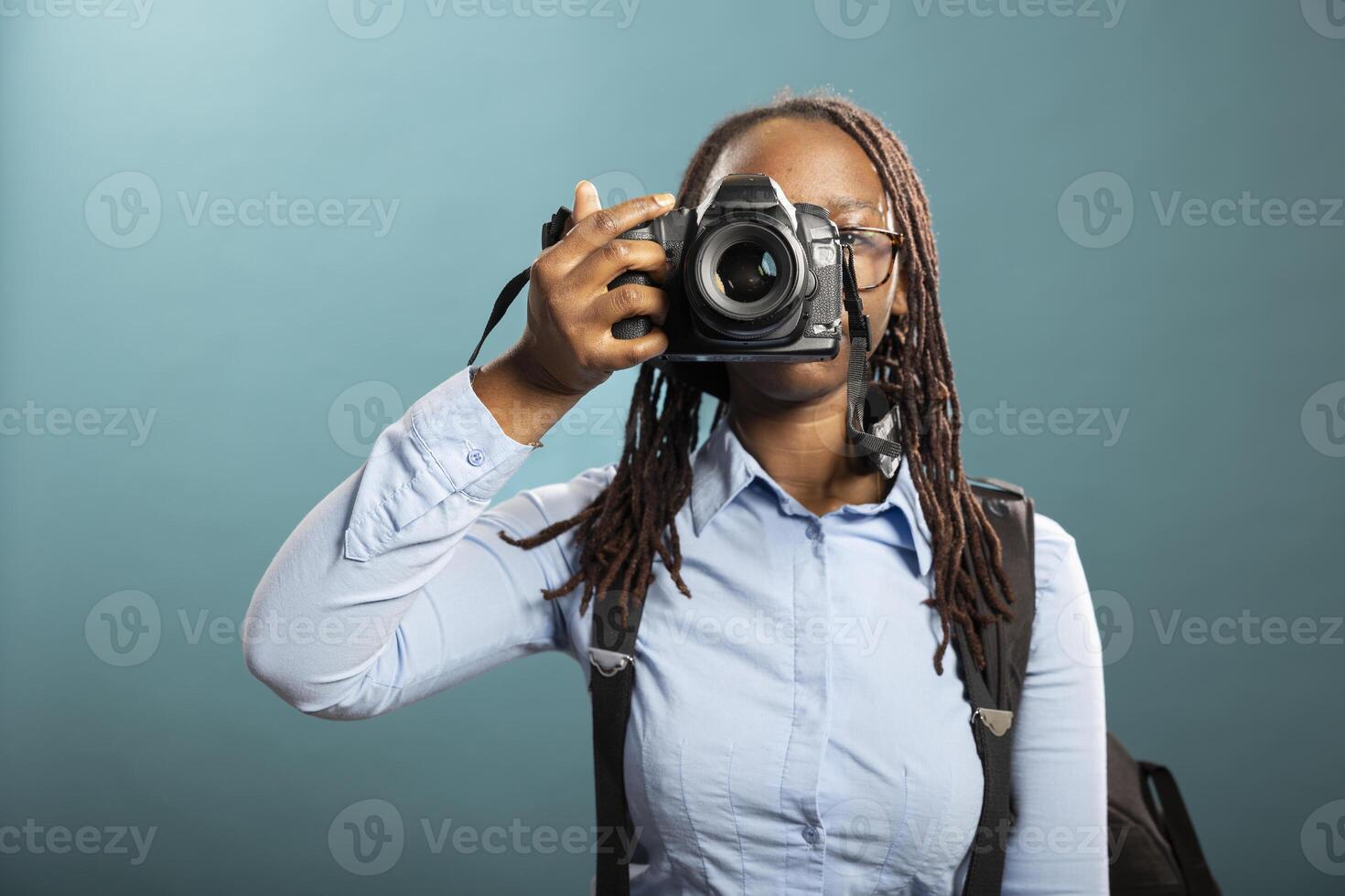 Portrait of black female photographer holding her DSLR, ready for client shoot, showcasing her professionalism. African american woman standing with camera, taking a shot in modern studio. photo