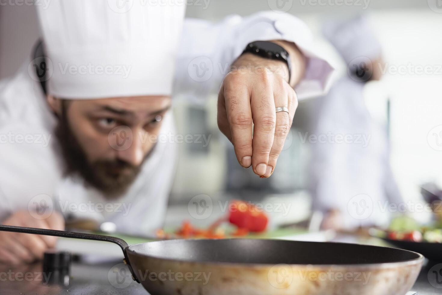 Focused male cook garnishing a dish with freshly cut vegetables on the stove, ensuring each plate meets gourmet and fine dining standards. Young head chef sprinkling bell pepper slices. photo