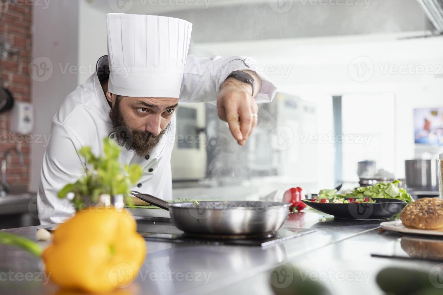 Head chef in restaurant kitchen adds a final touch of herbs to plated dish, using fresh greenery and spices to elevate the flavors while cooking the meal on the stove. Delicious culinary arts. photo